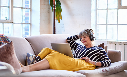 A woman on a her computer and laying on a sofa